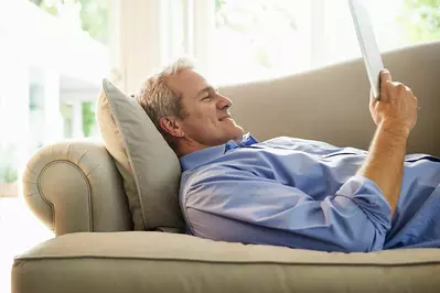 man laying on the couch reading while smiling