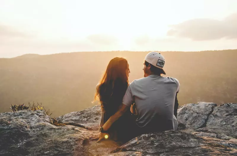 couple sitting together on a mountain ledge at sunset