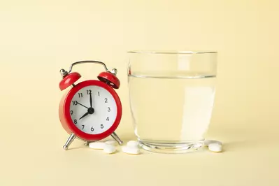 Photo of a clock with medicine and a glass of water