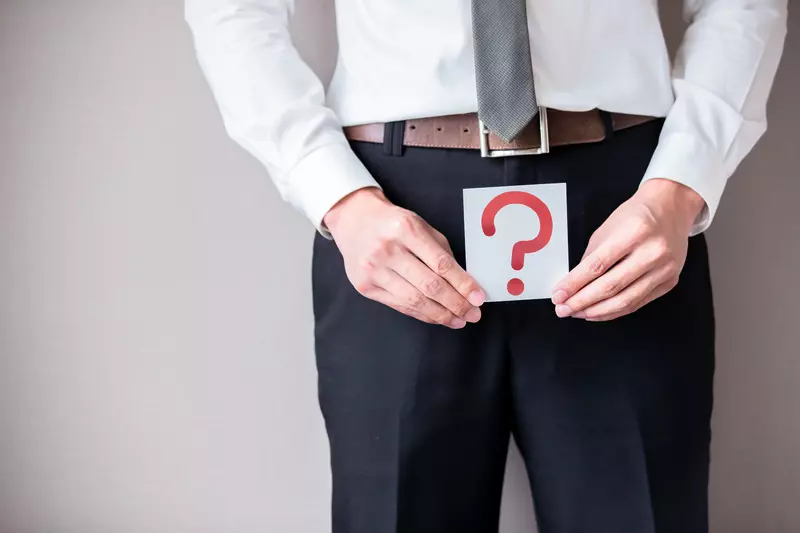 Man in Suit Holding Sign with a Question Mark In Front of His Lower Body