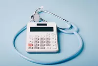 A simple handheld calculator with a blue stethoscope encircling it to illustrate medical costs