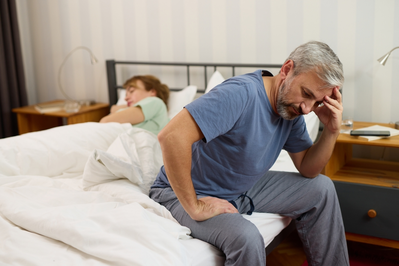 older man sitting on edge of bed upset